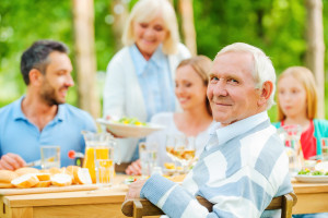 Enjoying time with family. Happy family of five people sitting at the dining table outdoors while senior man looking over shoulder and smiling